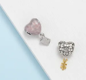 Macro-opname van zilveren puzzel-hartbedel en gouden hanger met YOU gravure voor DIY armband