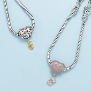 Detailopname van zilveren slangkettingarmbanden met roze hart- en envelopbedeltjes