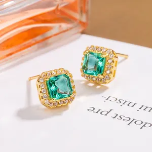 Detail of square green zircon stud earrings with a gold-plated halo setting on a card