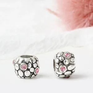 Macro detail of silver beads with vintage texture and pink rhinestones on white surface