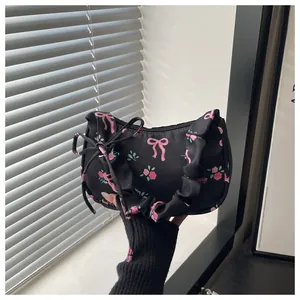 Detail of black satin handbag with pink bows and pleated handle held by model
