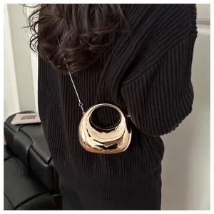 Detail of a hollow gold crescent handbag with a glossy metallic mirror finish on a model