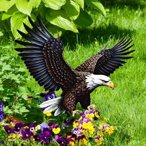 Detail of a lifelike bald eagle garden stake sculpture landing in a green flower bed