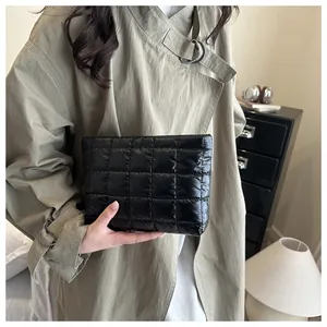 Close-up of black quilted puffer cosmetic bag held by a model wearing a beige trench coat