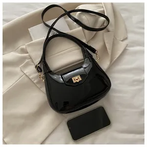 Detail der glänzenden schwarzen Hobo-Tasche mit goldenem Drehverschluss und Smartphone