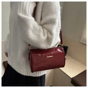 Detail of dark red cylinder crossbody bag with golden FASHION logo on white sweater