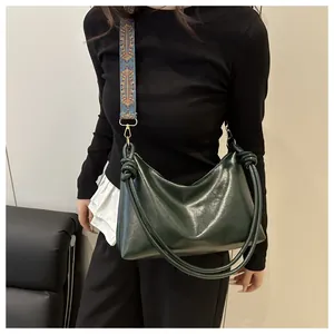Detail view of dark green hobo bag featuring polished leather and woven floral strap