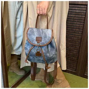Detailed view of gray-blue backpack featuring brown leather trim and metal hook closure