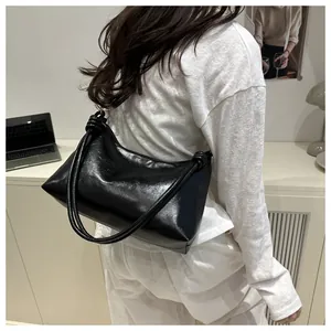 Close-up of a black glossy PU leather hobo bag with unique knotted shoulder strap detail