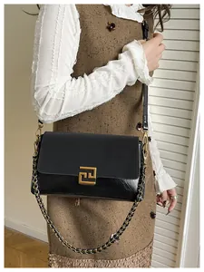 Detail of a black leather handbag with golden geometric lock on brown knit dress