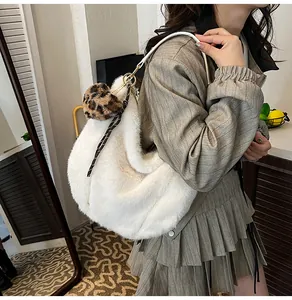 Detail of white plush shoulder bag with leopard pompom and ribbon on beige outfit