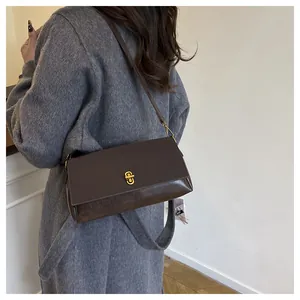 Close-up of stylish brown rectangular bag with a golden turn-lock clasp on a grey coat