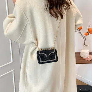 Fashionable black embroidered crossbody bag with gold chain strap on minimalist background