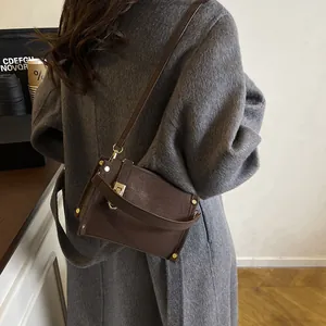 Deep brown lychee textured crossbody bag with gold hardware worn over a grey coat
