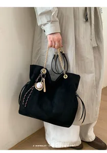 Dettaglio della borsa tote in pelle scamosciata nera con catena d'oro e ciondolo baseball