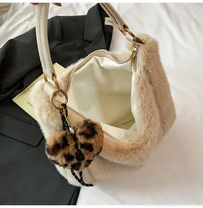 Detail of off-white plush tote bag with leopard heart charm and gold zipper on white bedding