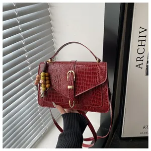 Detail of dark red croc-embossed leather bag with golden clasp and beaded accessory