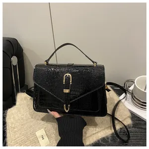 Detail of glossy black crocodile pattern handbag with elegant gold U-shaped buckle