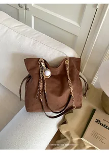 Dettaglio della borsa tote in pelle scamosciata marrone con catena dorata e charm