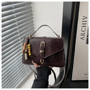 Detail of crocodile embossed crossbody bag with vintage gold buckle and beaded tassel accessory