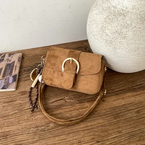 Retro brown suede shoulder bag with gold horseshoe buckle and baseball charm on a table