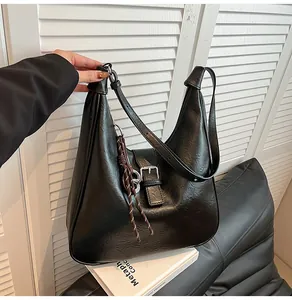 Detail of black leather crescent shoulder bag with metallic buckle and woven pendant
