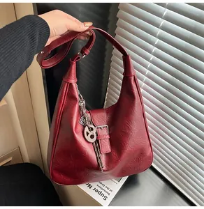 Detail of burgundy tote bag with leather texture and silver metal hanging charm decoration