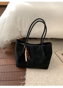 Close-up of black suede tote bag with a retro beaded tassel charm on a cozy rug