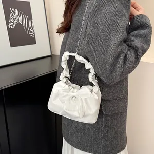 Weiße Handtasche mit gerafftem Griff und Schleife, getragen von Model im grauen Mantel