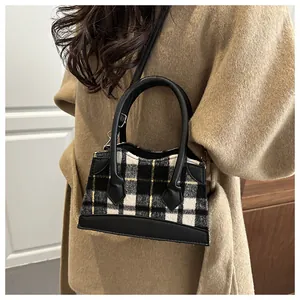 Gros plan d'un sac seau en tweed à carreaux porté avec un manteau en laine beige