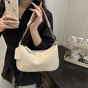 Sac sous le bras tressé crème avec chaîne dorée porté par un mannequin dans un café