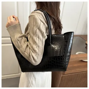 Detailed side view of black crocodile pattern tote bag held by model in casual outfit