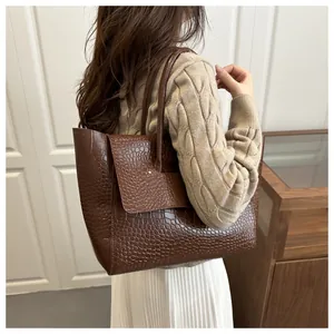 Detail of dark brown tote bag featuring glossy crocodile texture and sturdy top handles