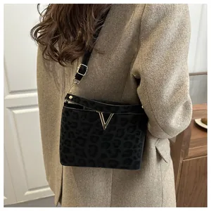 Detail of black leopard print crossbody bag with gold V hardware on beige wool coat