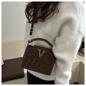 Close-up of leopard print crossbody bag with gold V-buckle on white knitted sweater