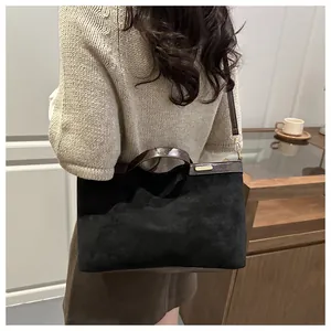 Détail d'un cabas en daim noir avec poignées en cuir marron et accents métalliques dorés