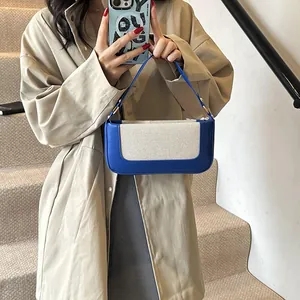 Detail view of blue leather and beige canvas contrast paneling on a modern shoulder bag
