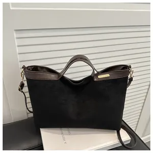 Détail du cabas en faux daim noir avec bordure en cuir marron et plaque dorée