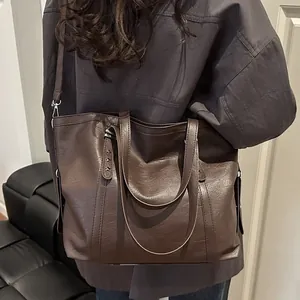 Large dark brown tote bag with litchi texture and star rivets shown on a model