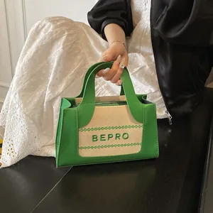 Detail van tweekleurige tas met groen leer en geborduurd BEPRO-logo op canvas