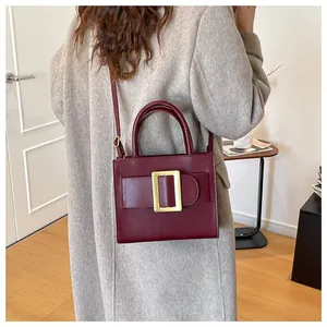 Chic burgundy leather handbag with gold buckle shown on shoulder of model in beige coat