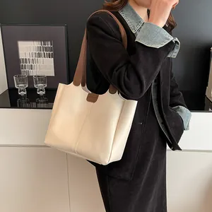 Detail view of cream tote bag featuring brown leather straps and vertical stitching detail