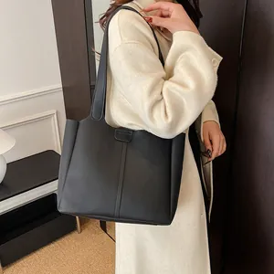 Close-up of a large black vintage leather tote bag with vertical stitching on a long coat