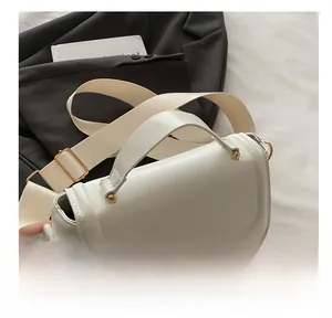 Detail showing the white crossbody bag with wide fabric strap and golden metal buckles