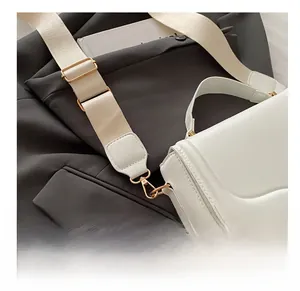 Detail of white crossbody bag with adjustable cream strap and gold hardware buckles