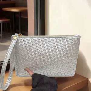 Silver woven leather clutch bag with wrist strap shown in a trendy cafe setting