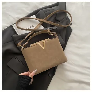 Detail of khaki suede crossbody bag featuring gold V-logo and structured top handle