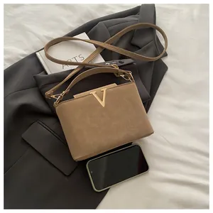 Detailed close-up of khaki shoulder bag with gold V-shaped metal logo on grey suit background