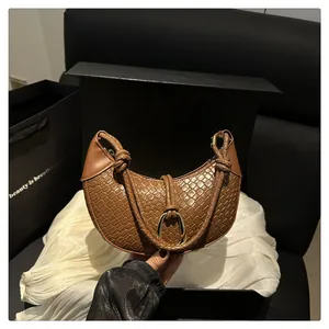 Détail d'un sac hobo tressé marron avec poignée nouée et fermoir doré sur soie