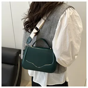 Detail of dark green leather crossbody bag with wave flap and wide woven strap